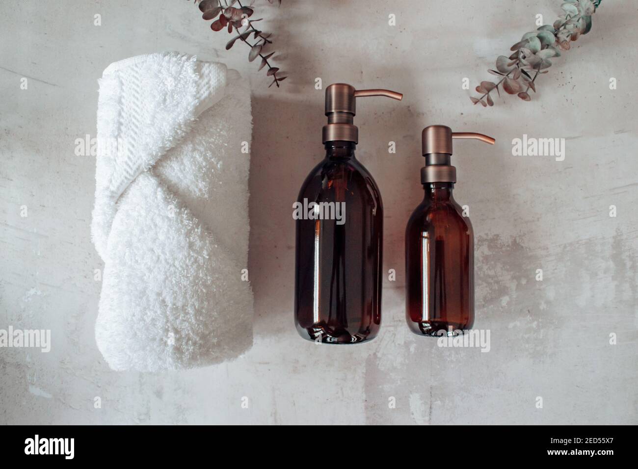 Amber glass shampoo or soap bottle dispenser with a copper steel pump against a stone background. Spa towel with eucalyptus. Stock Photo