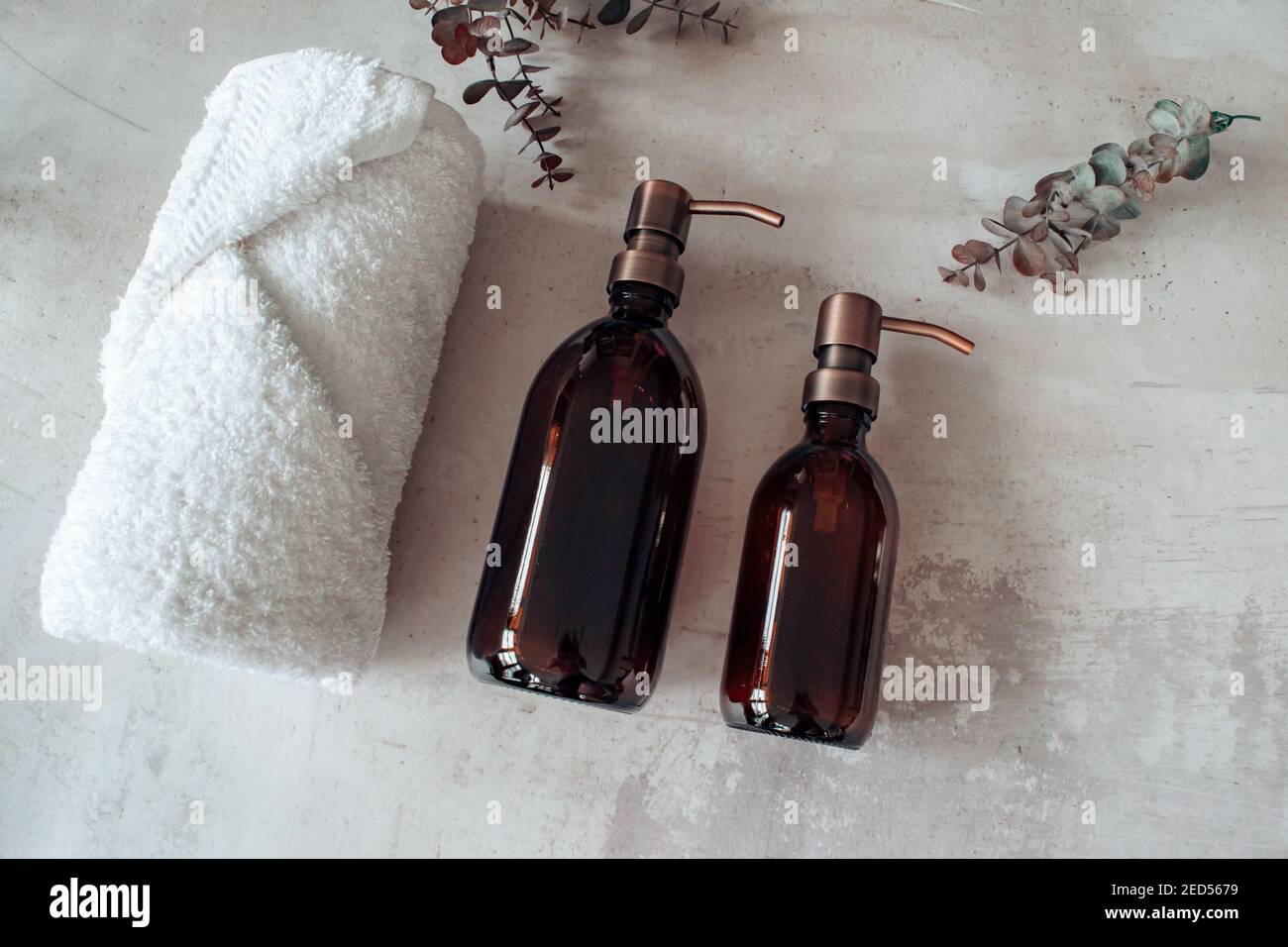 Amber glass shampoo or soap bottle dispenser with a copper steel pump against a stone background. Spa towel with eucalyptus. Stock Photo