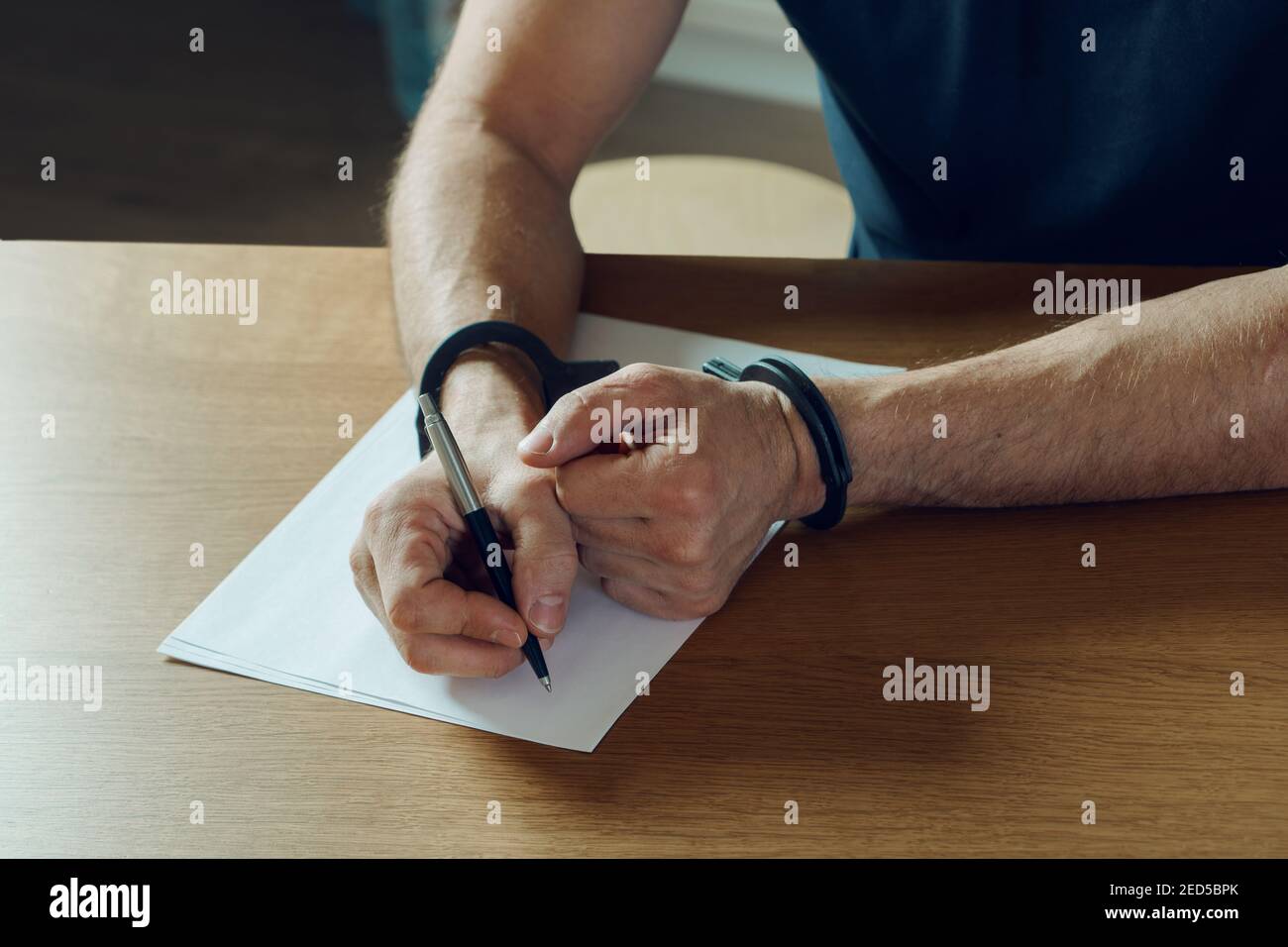 Men hands with handcuffs fill the police record, confession. on top of the police investigative detective. Arrest, bail, criminal, prison Stock Photo