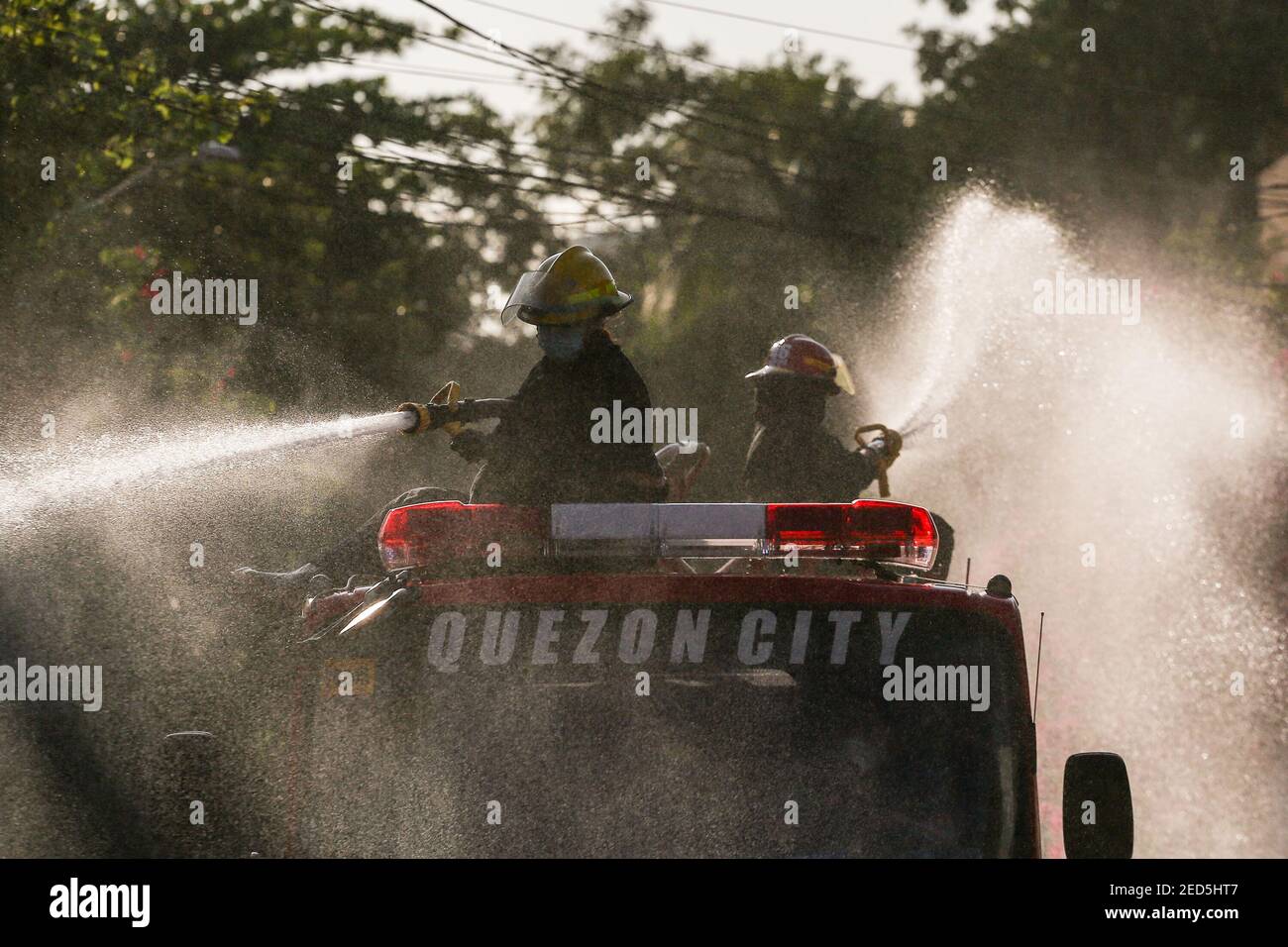 Fireman uses a hoses to spray disinfectant solution along a street to help curb the spread of COVID-19 during the coronavirus lockdown in Manila, Philippines. Stock Photo