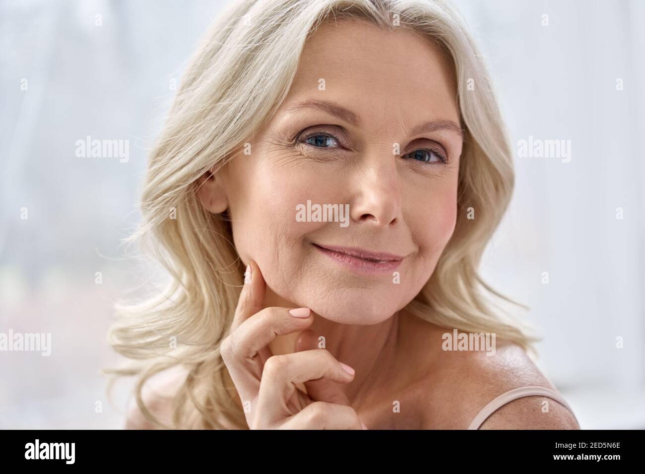 Smiling middle aged blonde woman looking at camera in bathroom. Stock Photo