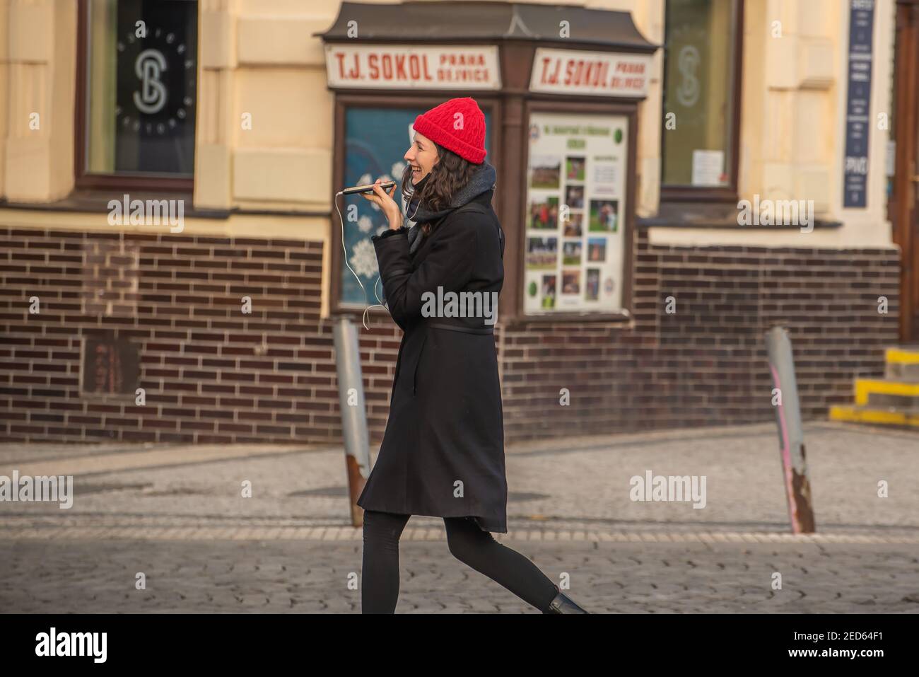 Prague, Czech Republic. 02-13-2021. Young trendy woman dress in black with red hat is laughing while speaking on the phone in the city center of Pragu Stock Photo