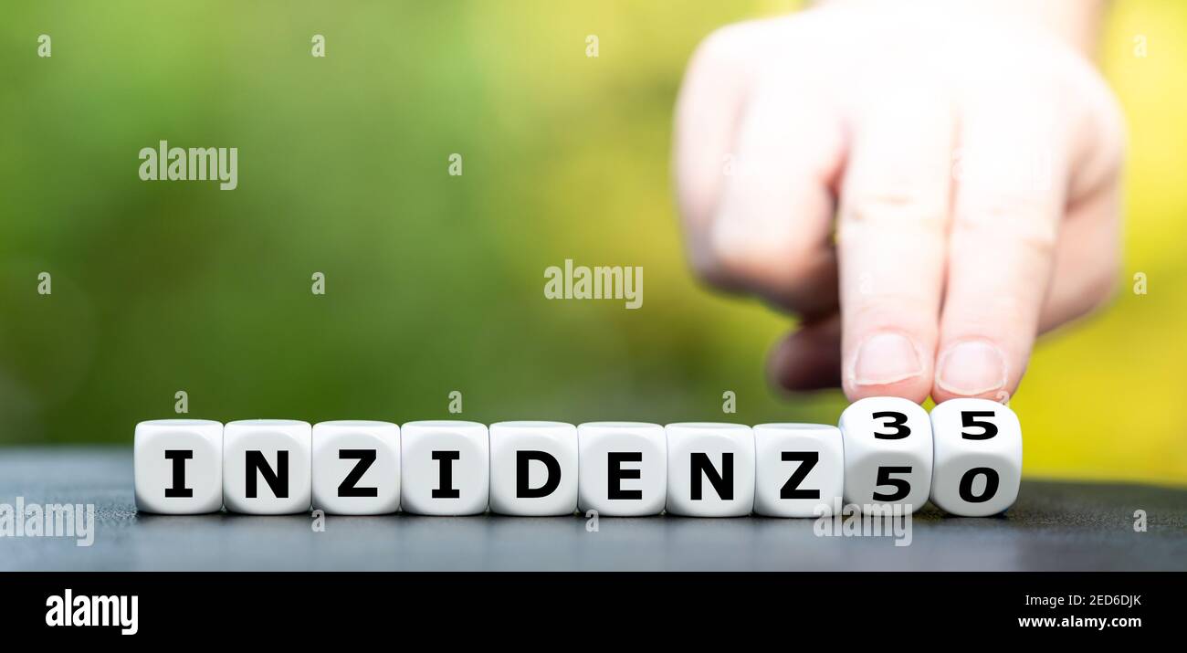 Hand turns dice and changes the German expression 'Inzidenz 50' (incidence 50) to 'Inzidenz 35' (incidence 35). Symbol for a new goal to archieve duri Stock Photo