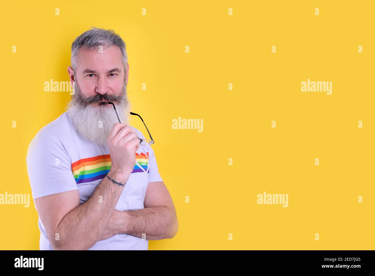Mature bearded man dressed with lgbtq symbols t-shirt looking at camera, studio portrait of homosexual man, yellow background Stock Photo