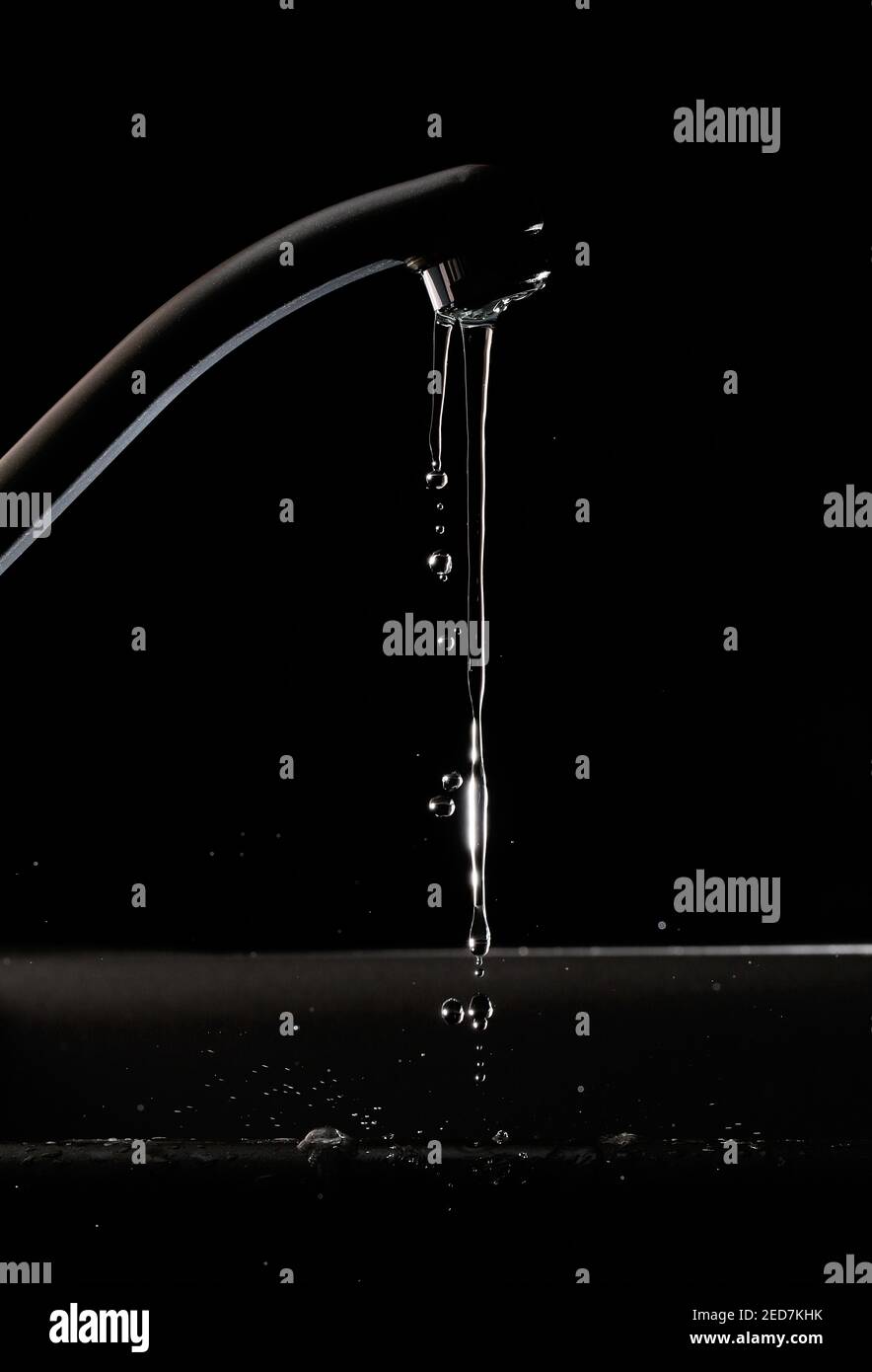 Leaking tap water against a black background, due to the tap being open Stock Photo