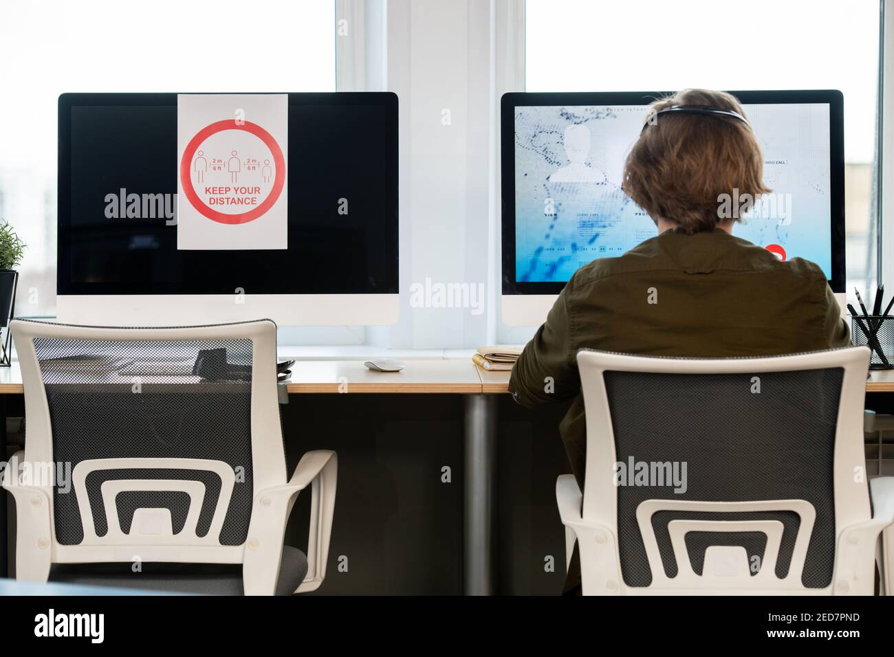 Rear view of male operator of call center sitting in front of computer ...