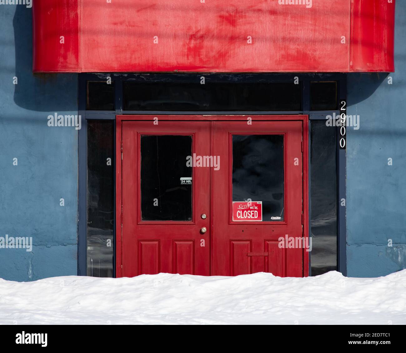Red doors entrance with a closed sign on a blue building blocked by a snow bank in Speculator, NY USA Stock Photo