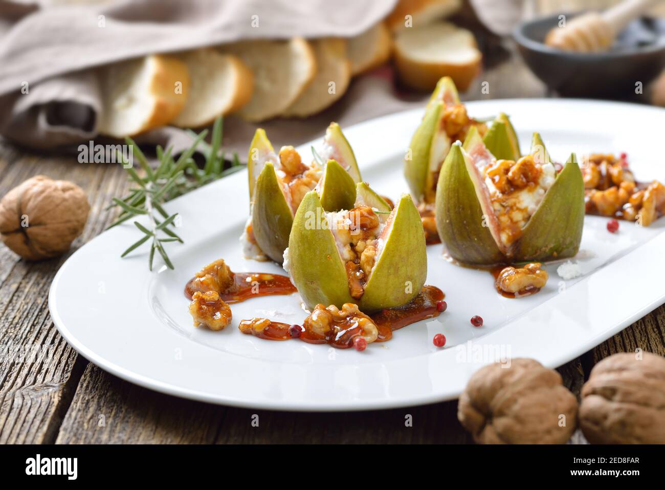 Baked figs stuffed with goats cream cheese and candied walnuts with sweet honey and rosemary Stock Photo