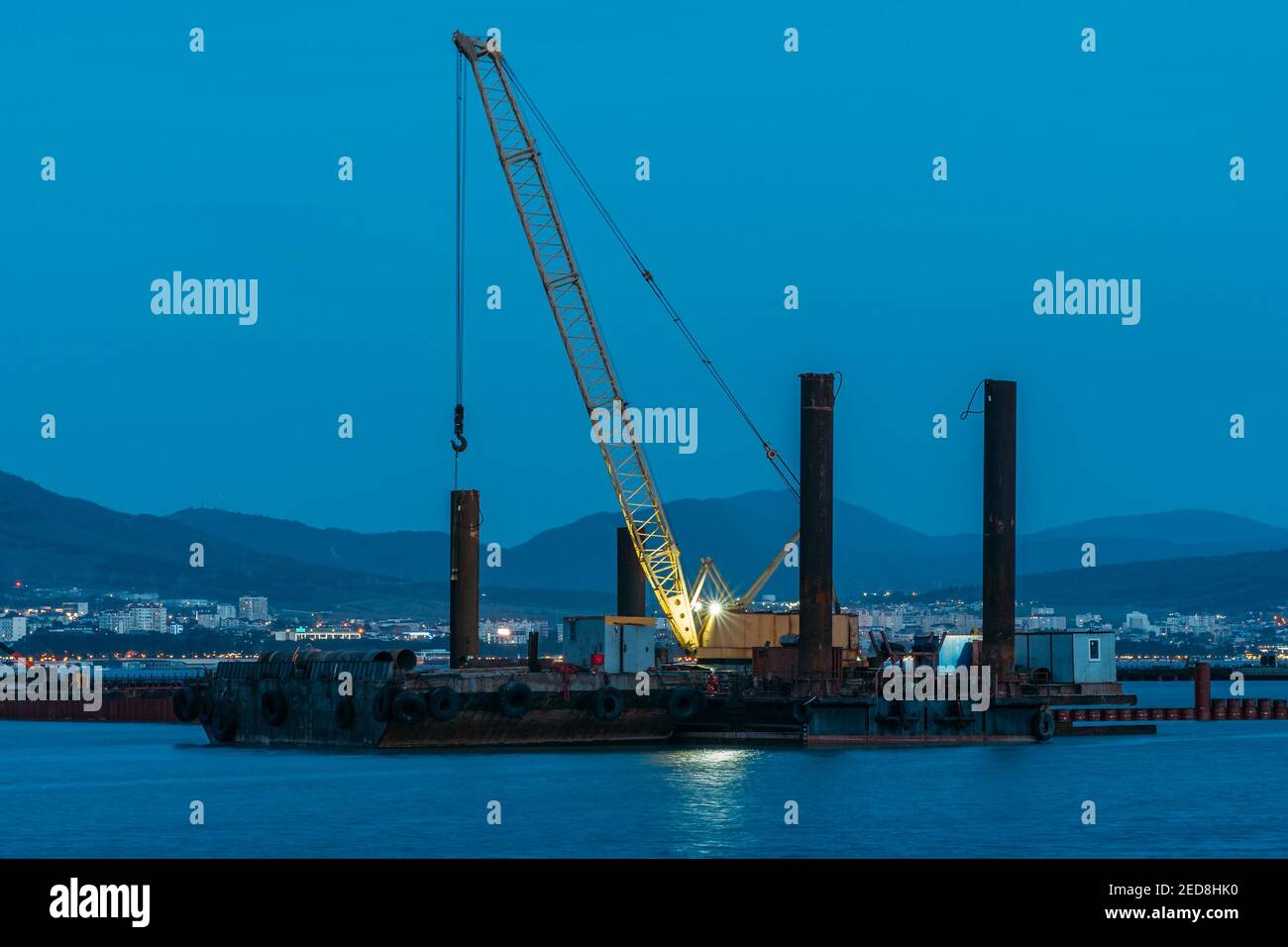 Cargo crane working in small port, construction of industrial harbor or dock in evening, sea goods transportation and logistic development concept. Stock Photo