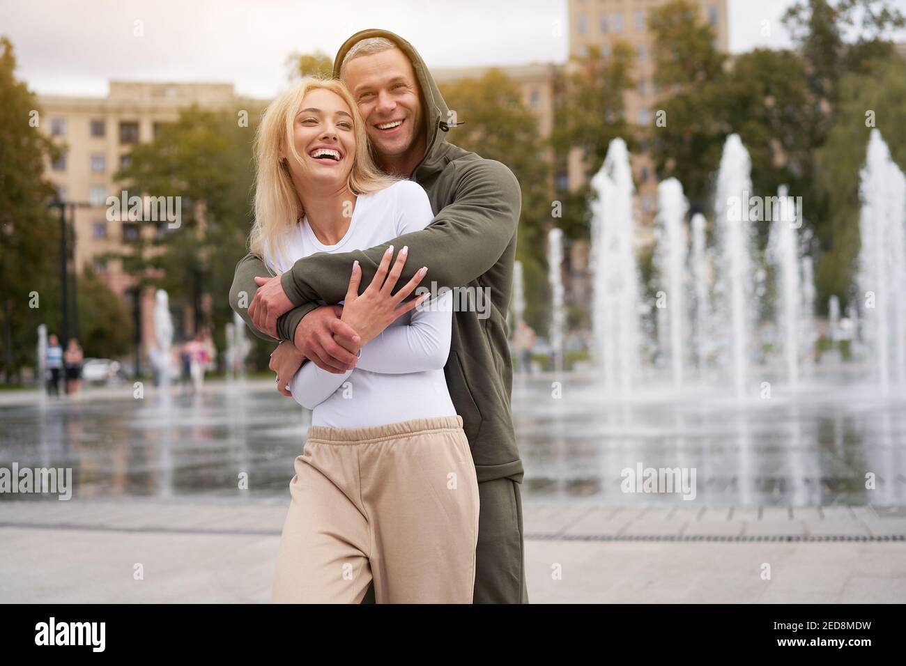 Couple in love walking outdoors park fountain Caucasian man woman walk outside after jogging dressed sport clothes Healthy livestyle dress up the hood Stock Photo