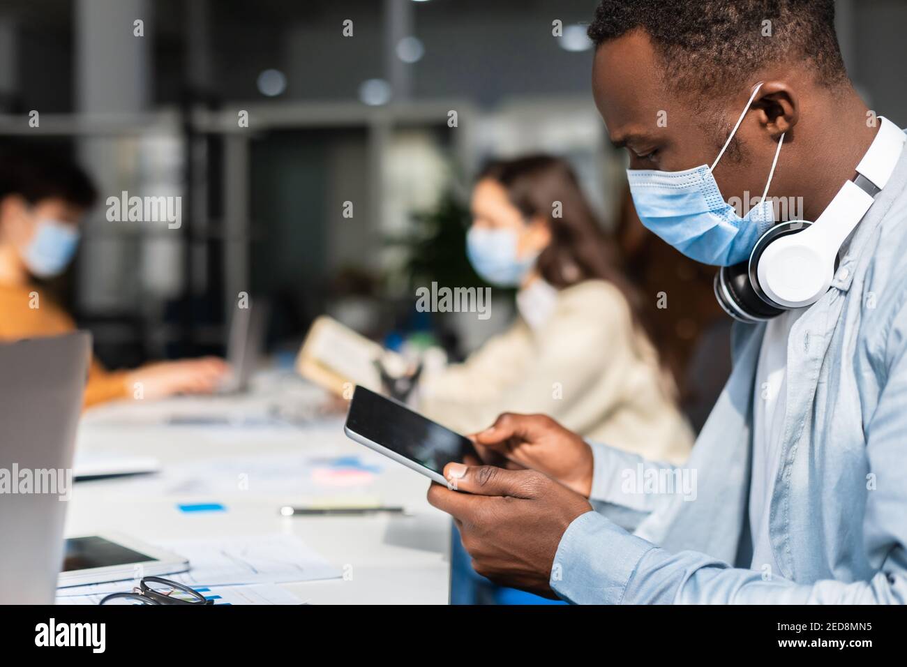 Black man in mask sitting at desk using tablet Stock Photo