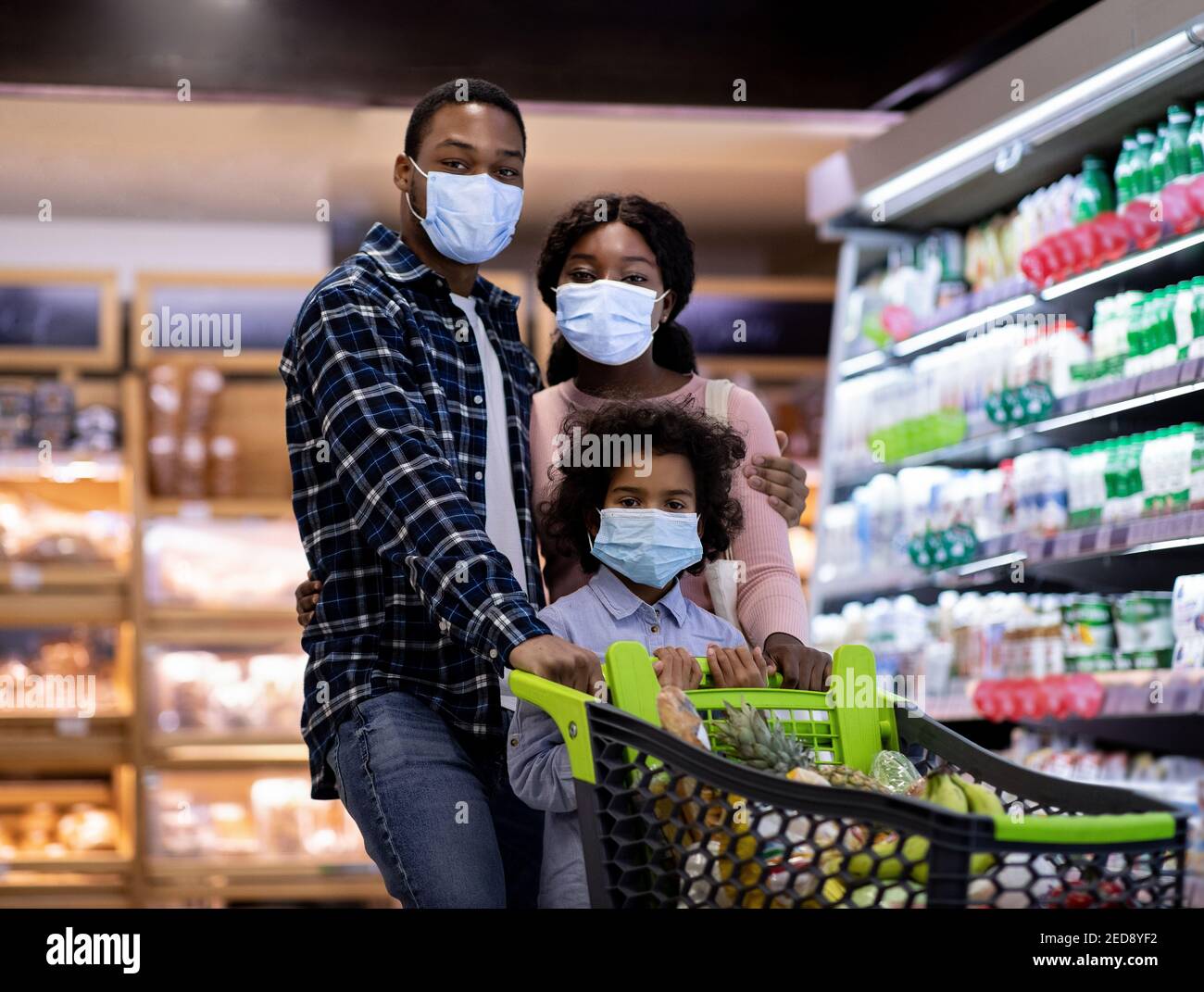 Young black family with child wearing face masks while shopping for ...