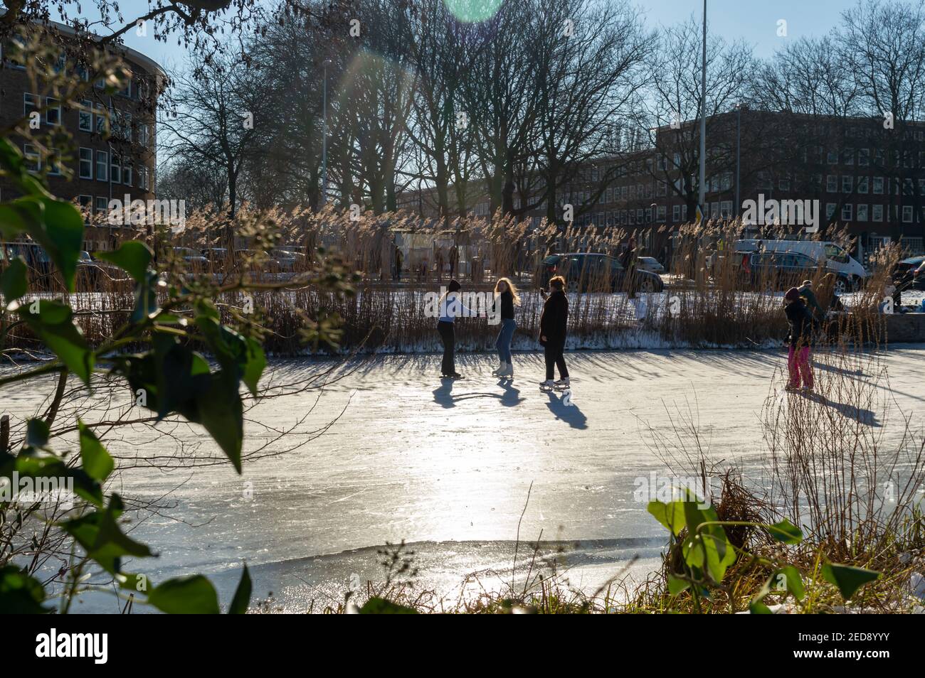 AMSTERDAM, THE NETHERLANDS, FEBRUARY 13,2021.Two girls ice skating on the canals of Amsterdam West, The Netherlands, in the late afternoon sun while a Stock Photo