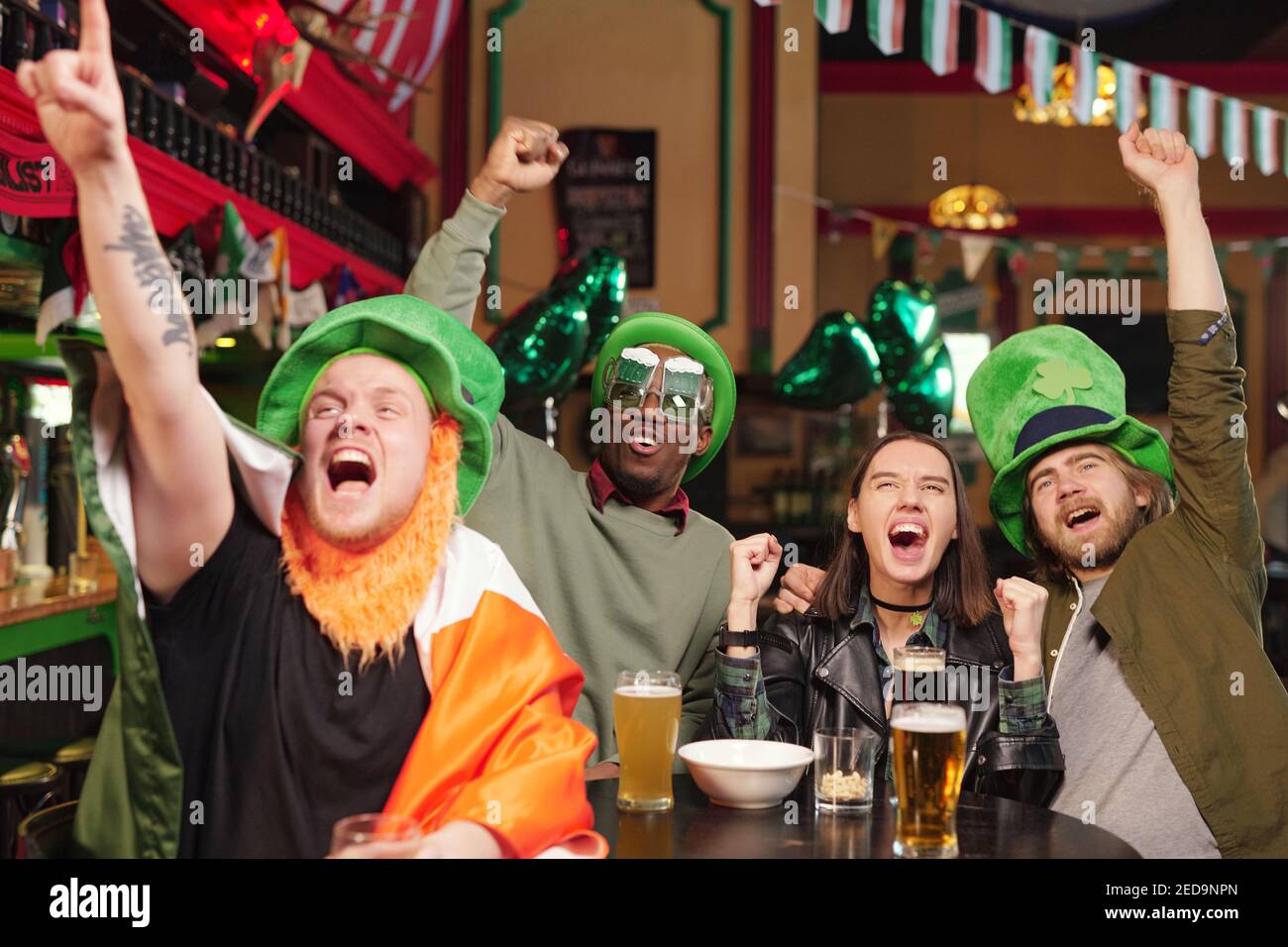 Group of young excited intercultural football fans in green hats and