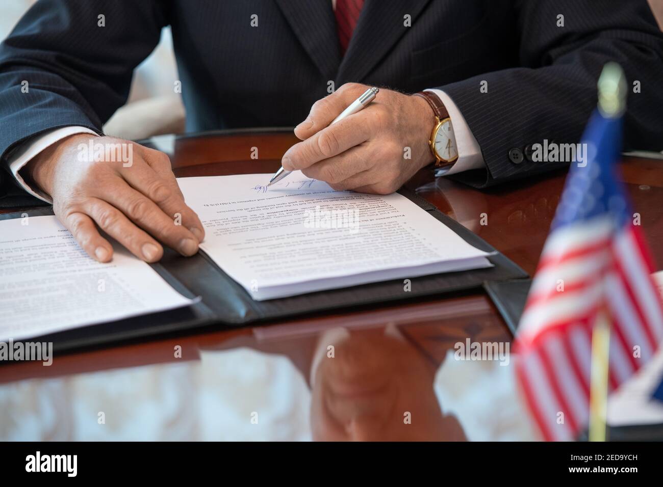 Hands of mature American delegate in formalwear signing contract of business partnership and pointing at signature while sitting by table Stock Photo
