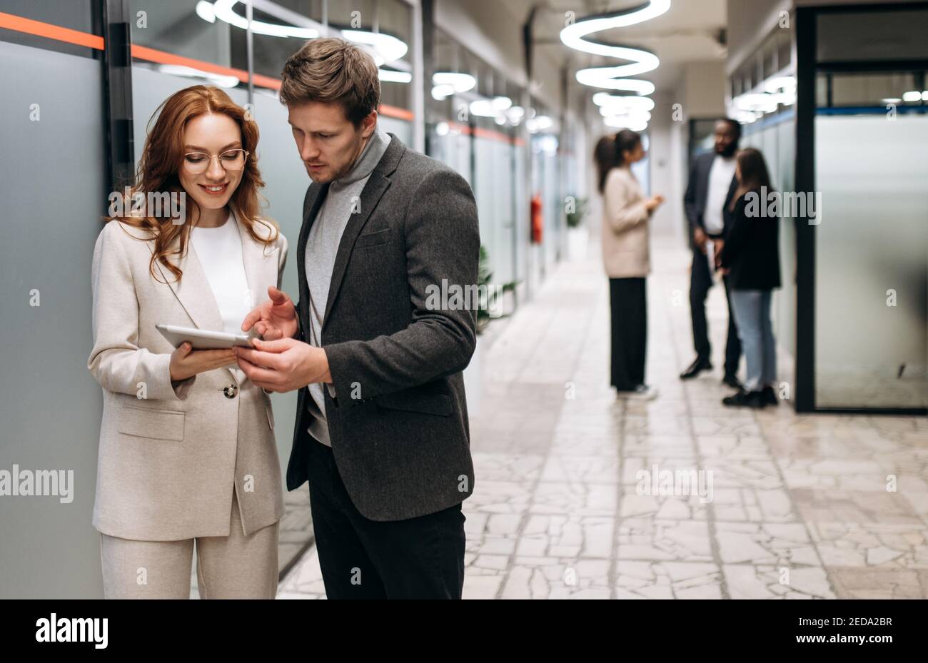Caucasian business partners at the workplace. Friendly colleagues cooperate to develop a startup or project together. Handsome man ask for advice from beautiful smiling woman, collaboration concept Stock Photo