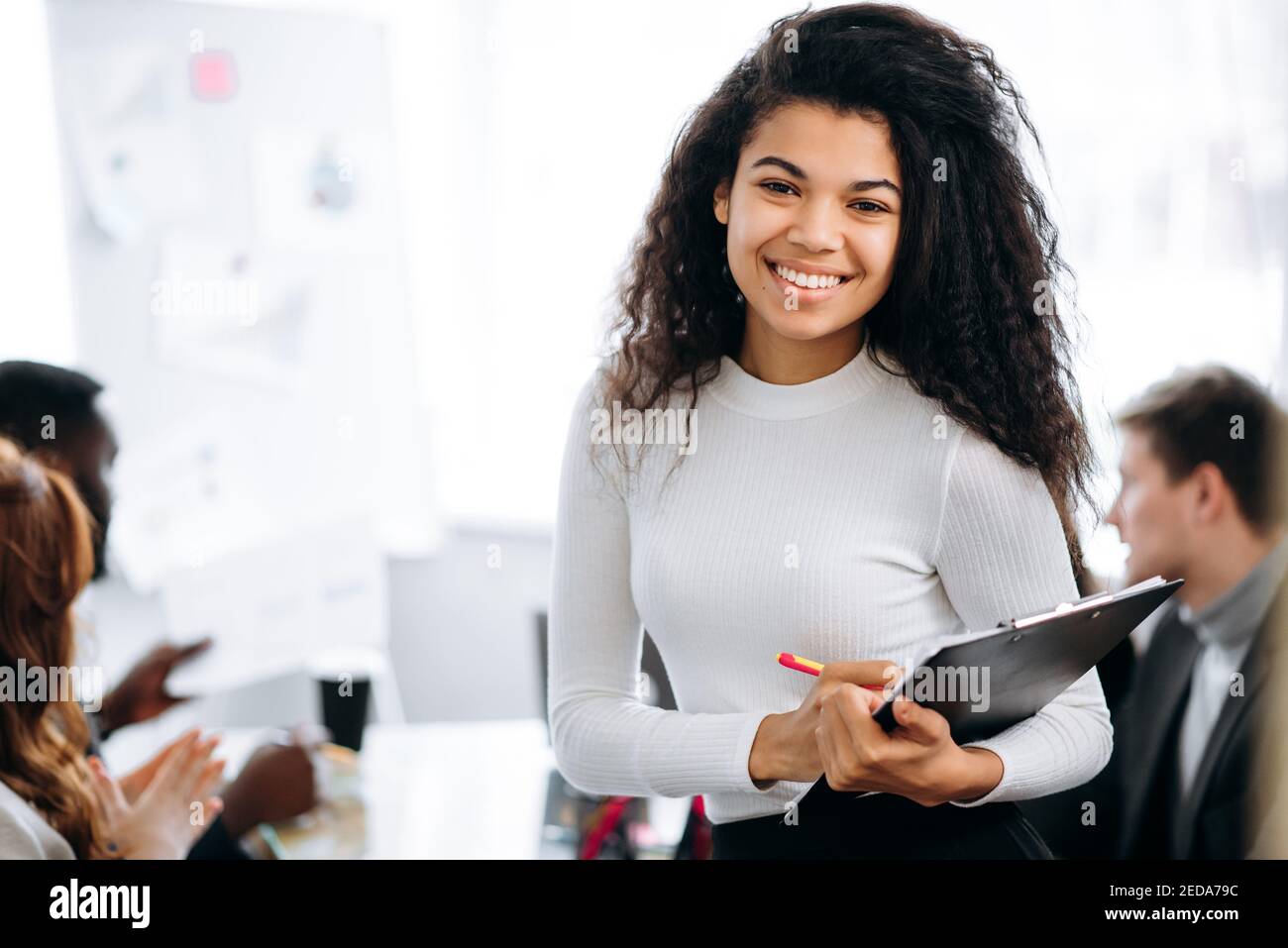 Portrait of african american female employee in formal wear at the workplace. Young business woman looks directly at the camera, smile. Successful woman at briefing meeting in office Stock Photo