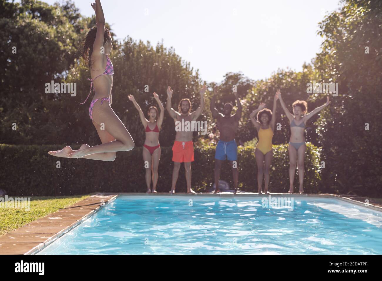 Diverse group of friends having fun and jumping into water at a pool ...