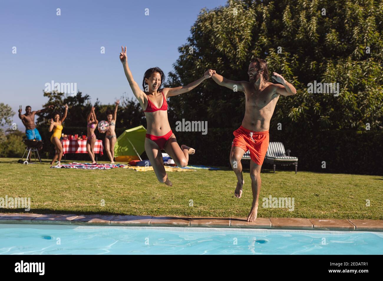 Diverse group of friends having fun and jumping into water at a pool ...