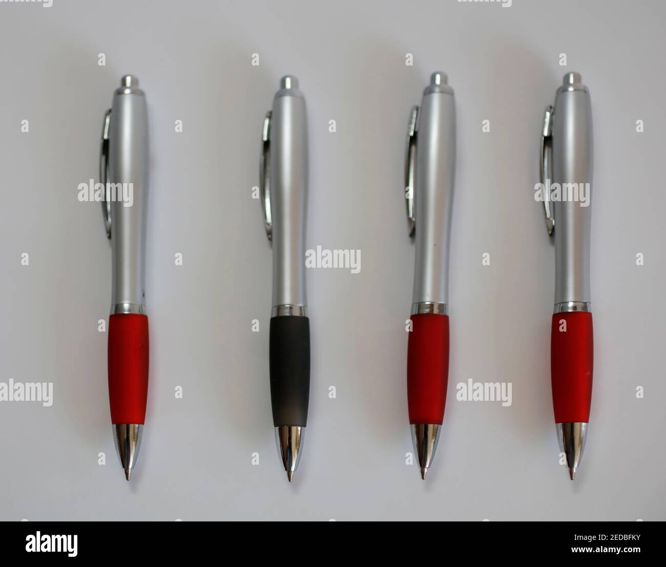 Three red ball point pens and one black one odd-one-out Stock Photo