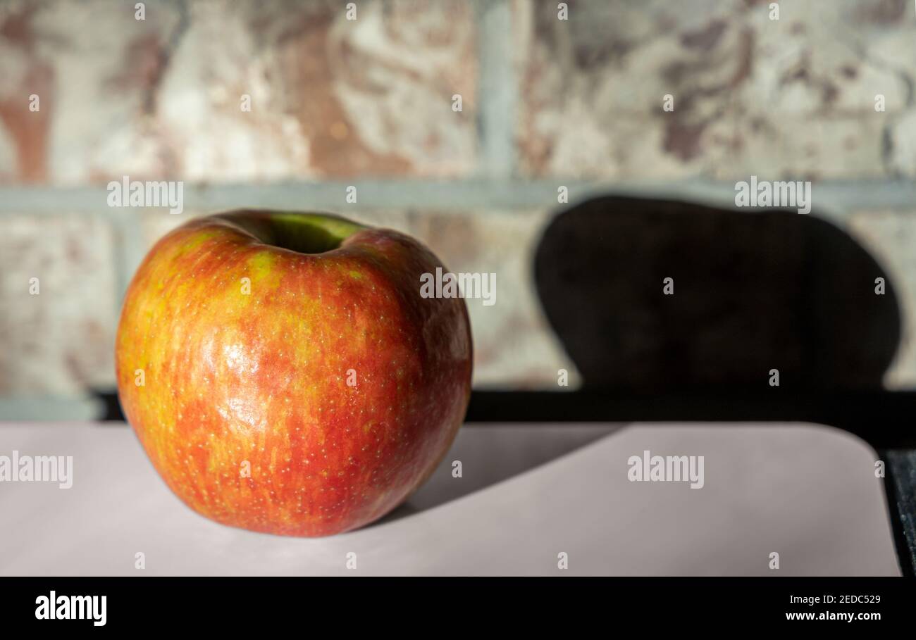 Big red apple on the white table against the brick wall Stock Photo