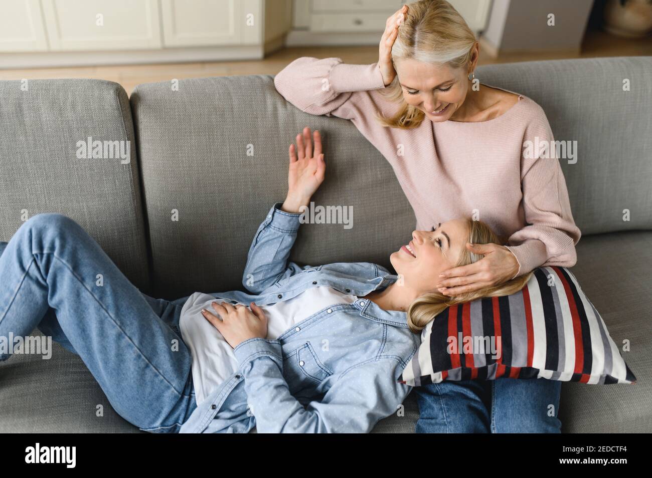 Mom and daughter relationship. Mature mom and young adult daughter chatting at home in the living room on the couch, sharing secrets, mom giving advice to her daughter Stock Photo