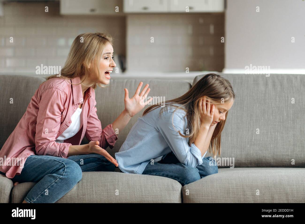 Angry mother scolding little daughter at living room, parent teaches a naughty mischievous child, kid girl feels upset about punishment and deprivation of entertainment Stock Photo
