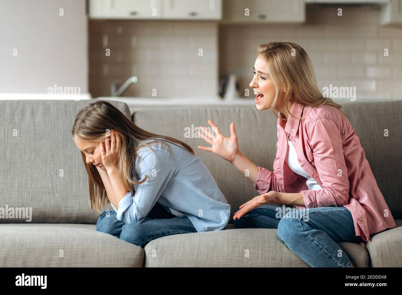 Conflict of mom and daughter. Screaming mother, shouts at little daughter scolding her. Little girl is ignoring mom, close her ears with arms. Complicated relationships of mother and child Stock Photo