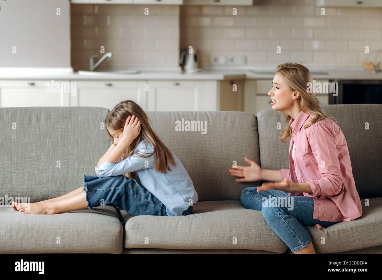 Side view, of screaming mother, shouts at little daughter scolding her. Little girl is ignoring mom, close her ears with arms. Complicated relationships of mother and child Stock Photo