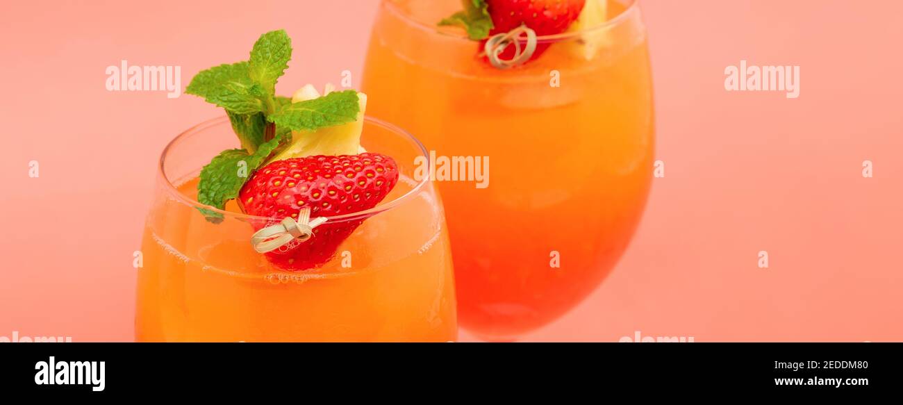 Colorful refreshing strawberry orange sunrise cocktail drinks in the glasses on coral pink banner background Stock Photo
