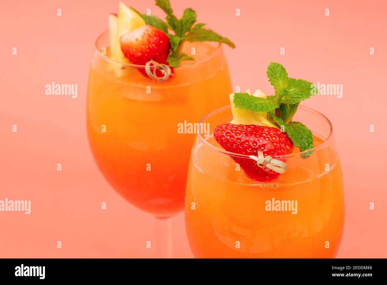 Closeup shot of colorful refreshing strawberry orange sunrise cocktail drinks in the glasses on coral pink background Stock Photo