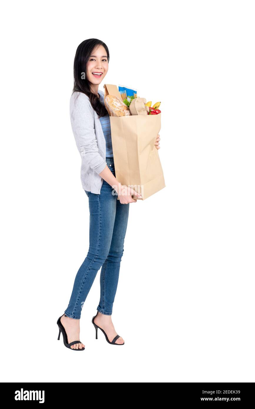 Beautiful smiling Asian woman holding paper shopping bag full of vegetables and groceries, studio shot isolated on white background Stock Photo
