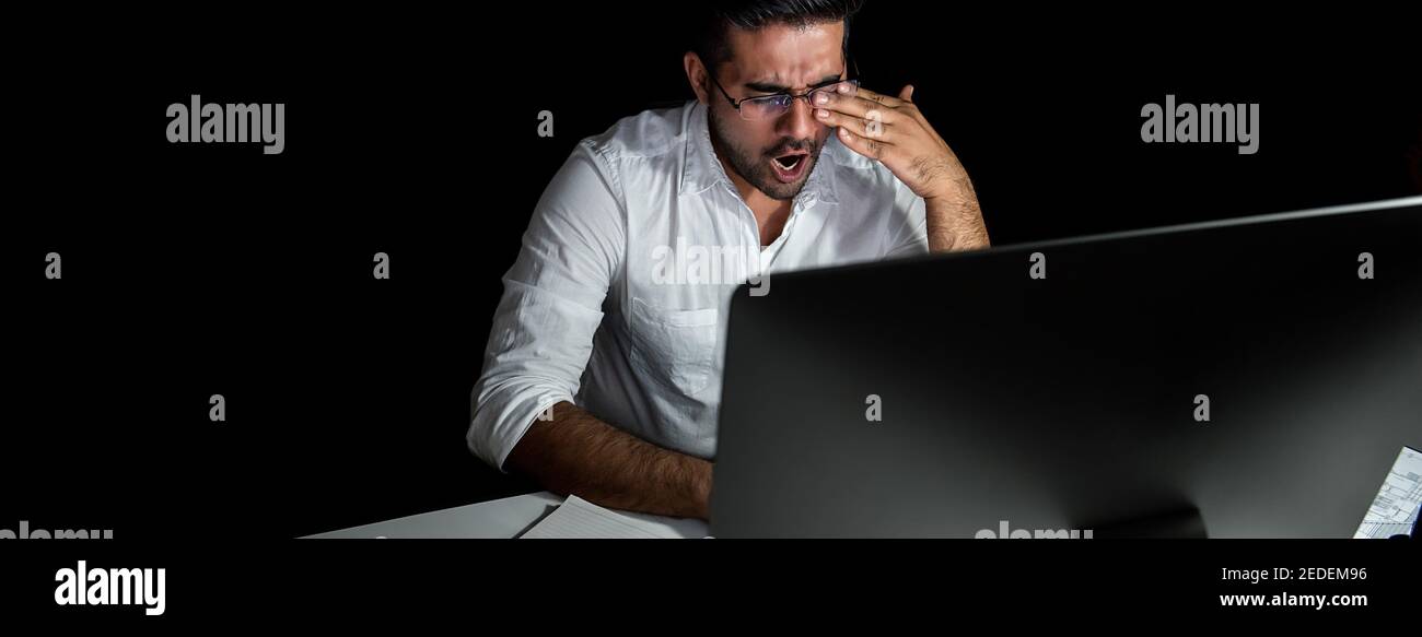 Tired fatigued Asian businessman feeling sleepy and yawning while working night shift in front of computer Stock Photo
