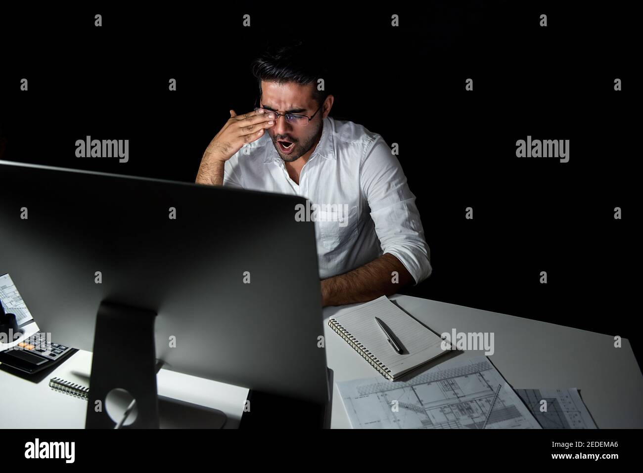 Tired fatigued Asian businessman feeling sleepy and yawning while working night shift in front of computer Stock Photo