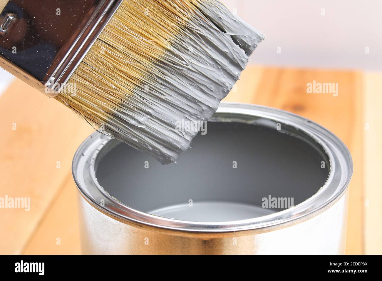 Brush with can paint in hand. A man paints wooden boards in a gray