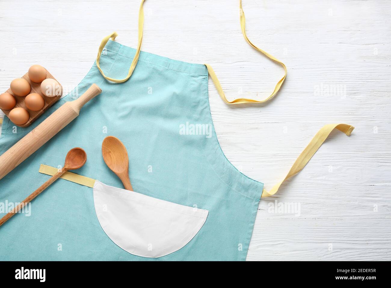 Clean apron, kitchen utensils and eggs on light background Stock Photo ...