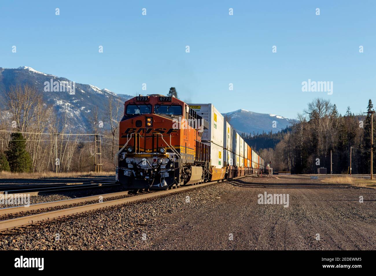 A trailing push locomotive, 6773, of a BNSF intermodal shipping container freight train coming down the tracks in the town of Troy, Montana. Stock Photo