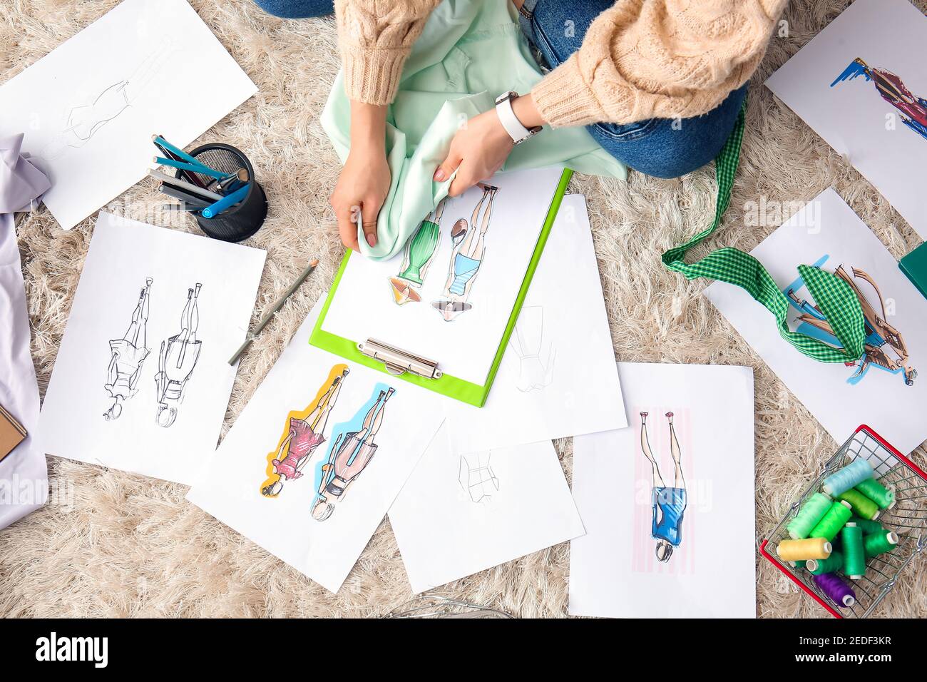 Female fashion designer working with sketches on carpet in studio Stock ...
