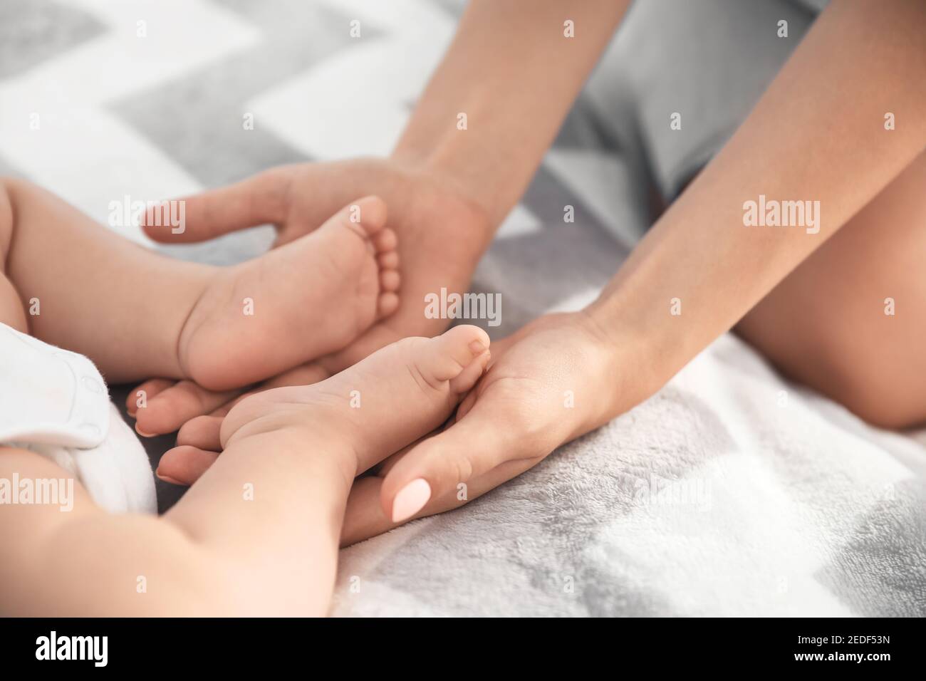 Mother holding feet of her little baby on bed Stock Photo