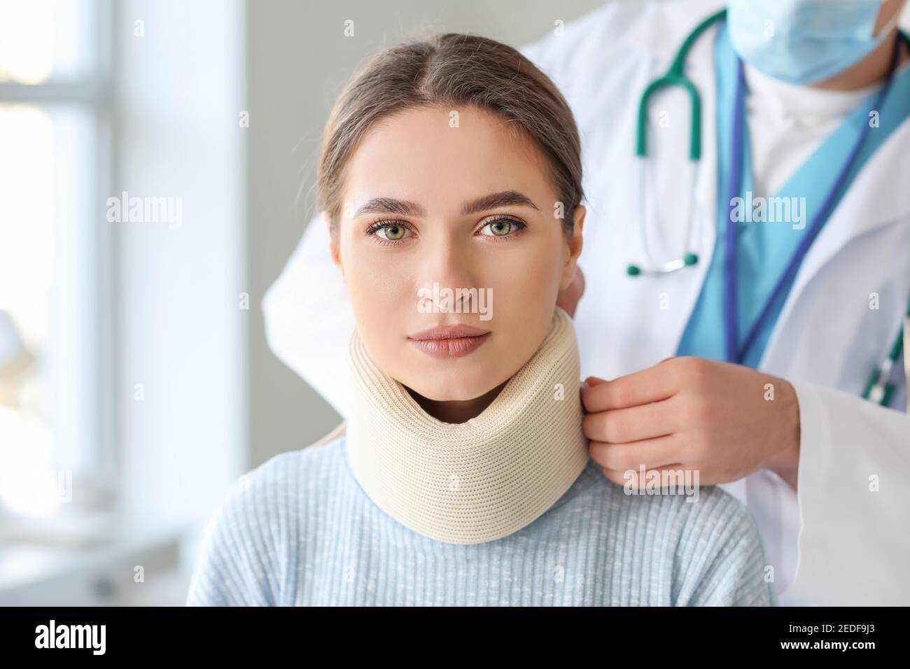 Doctor applying cervical collar on neck of young woman in clinic Stock