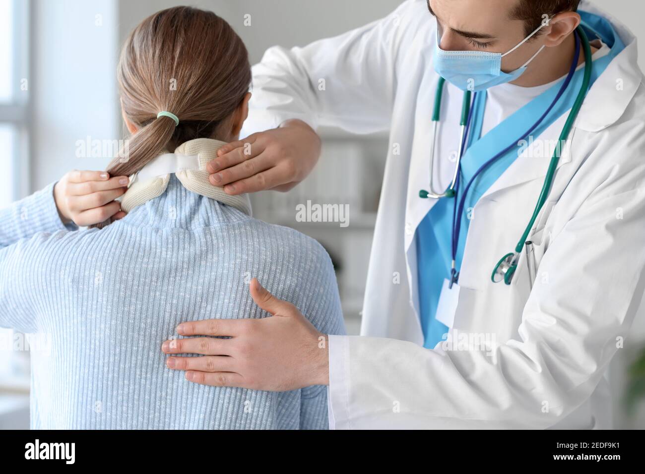 Doctor applying cervical collar on neck of young woman in clinic Stock