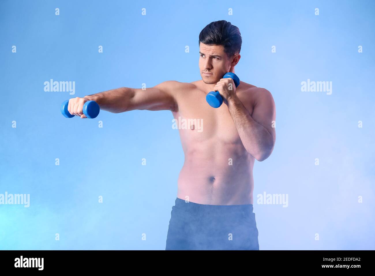 Sporty young man training with dumbbells on color background Stock Photo