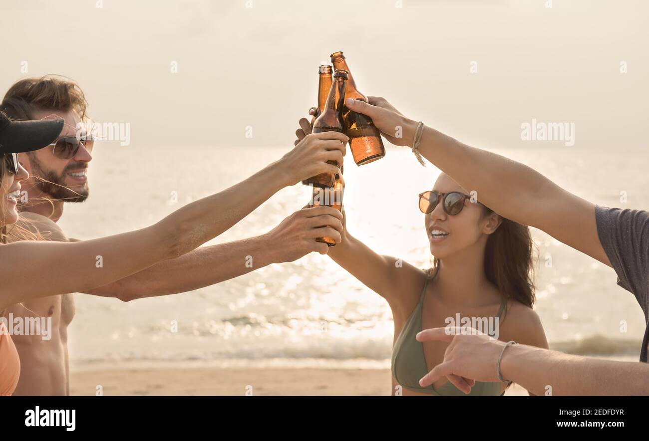 Group of friends having celebration party claging beer bottles making a toast before drinking at the beach in twilight Stock Photo