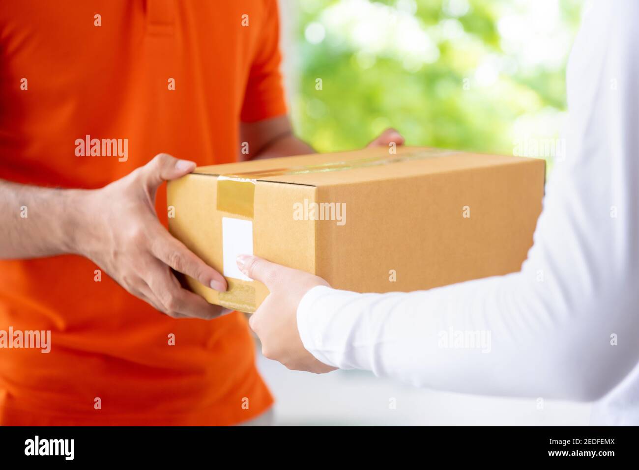 Courier service delivery man in orange uniform giving parcel box to customer at home Stock Photo