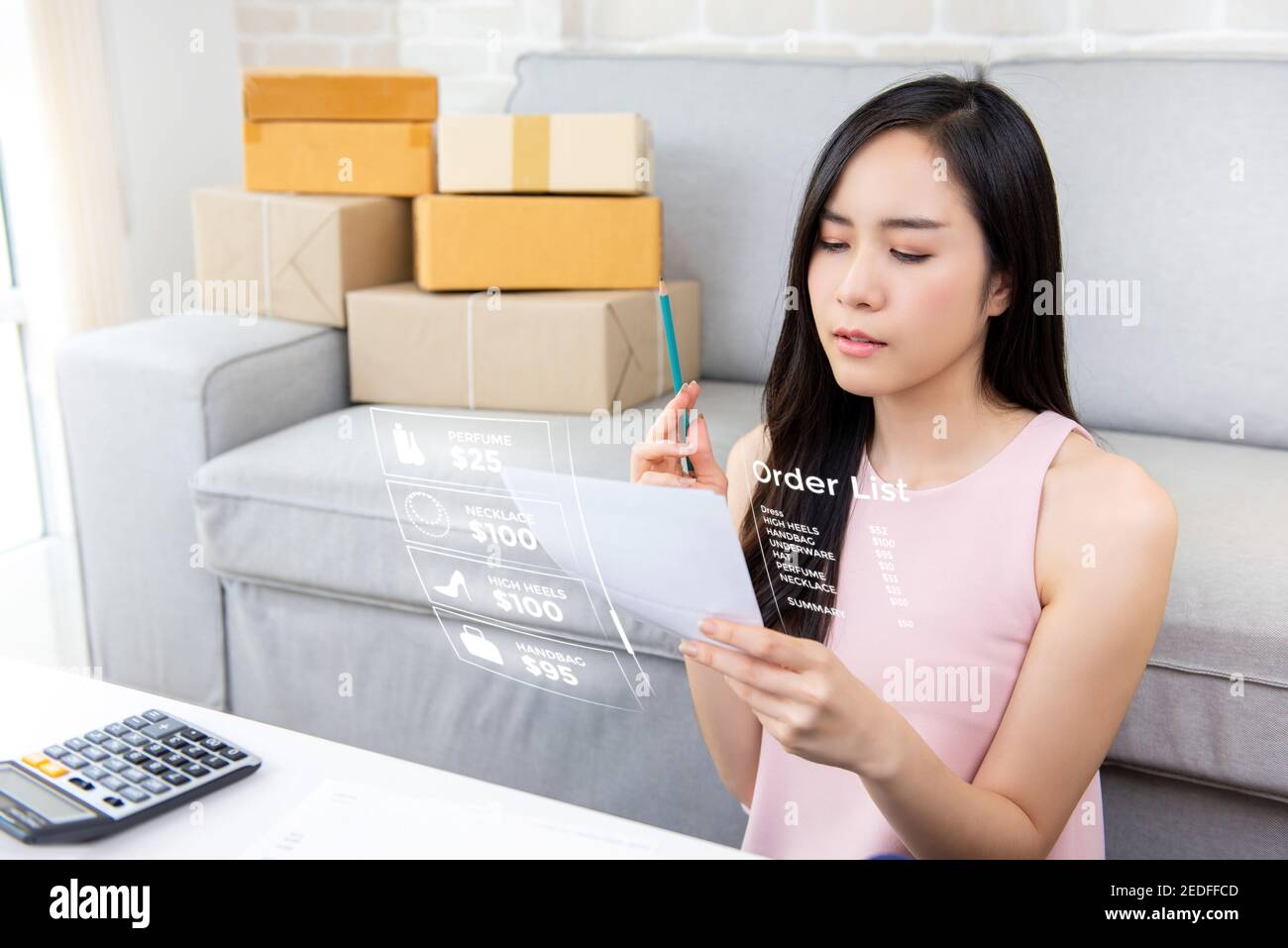 Young Asian woman entrepreneur or freelance online seller working at home checking orders preparing for delivery packages to customers Stock Photo