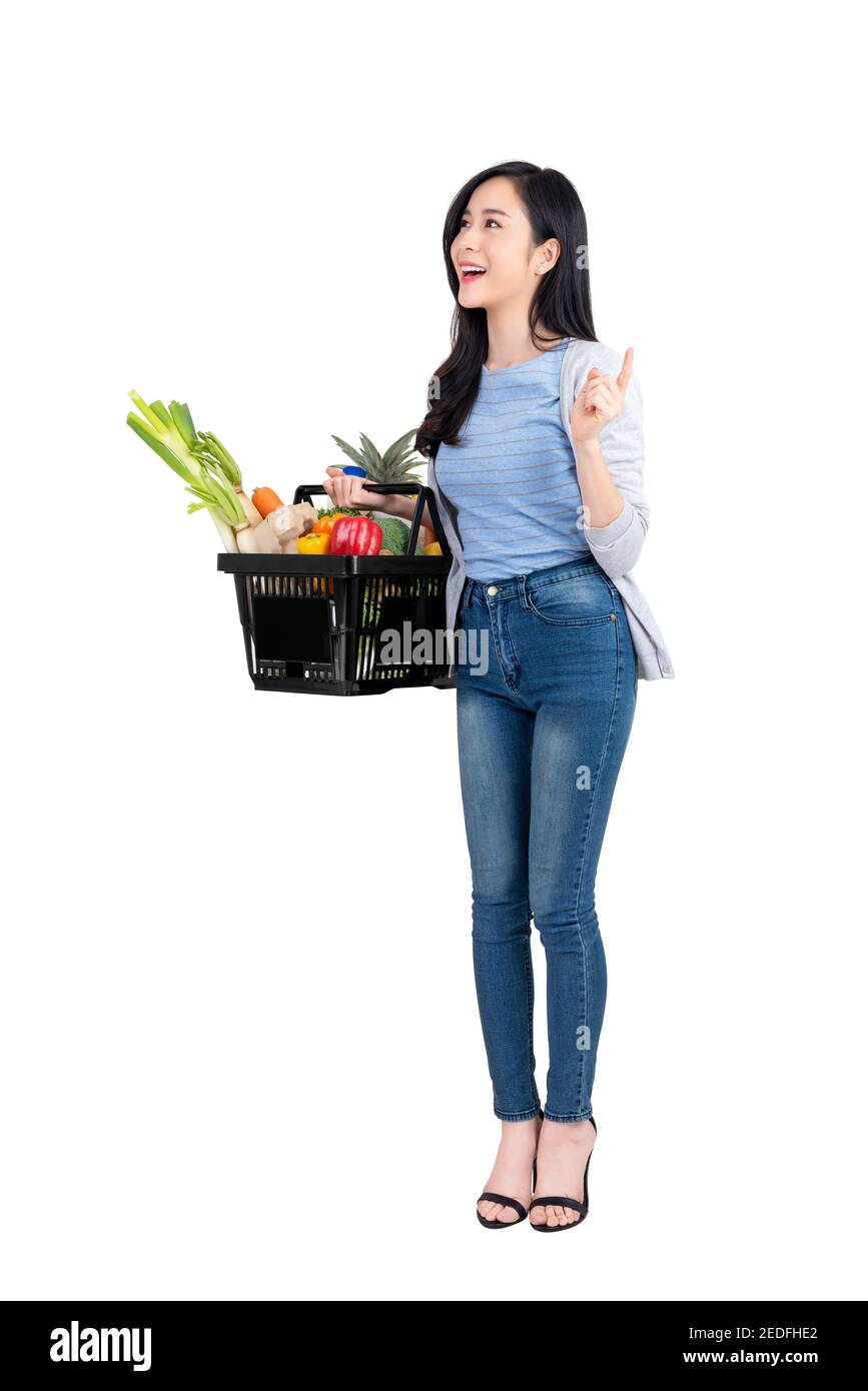 Beautiful Asian woman holding shopping basket full of vegetables and groceries, studio shot isolated on white background Stock Photo