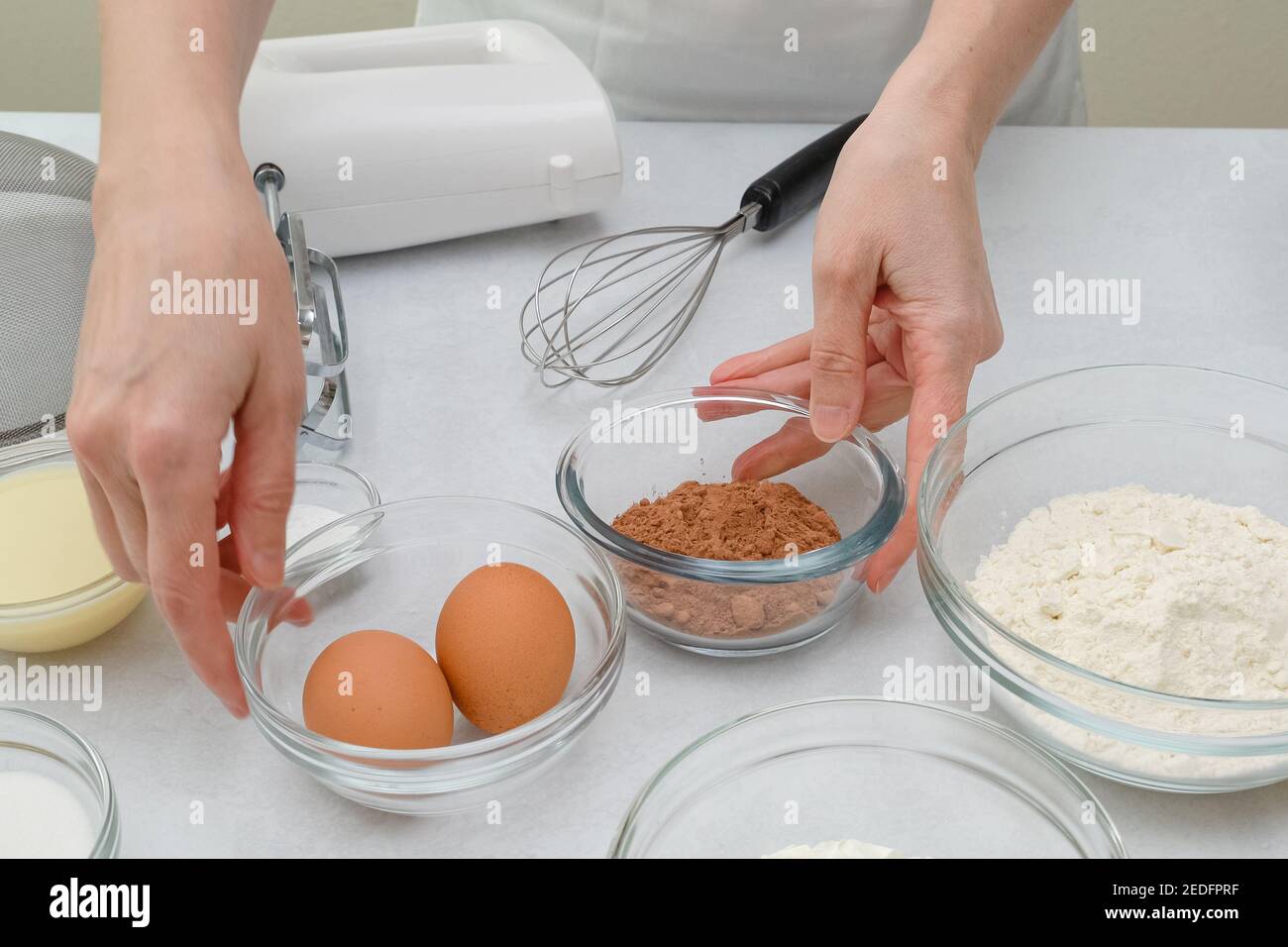 Ingrediets and dishes for making chocolate cake close up on kitchen table. Step by step chocolate cake recipe, woman hands Stock Photo