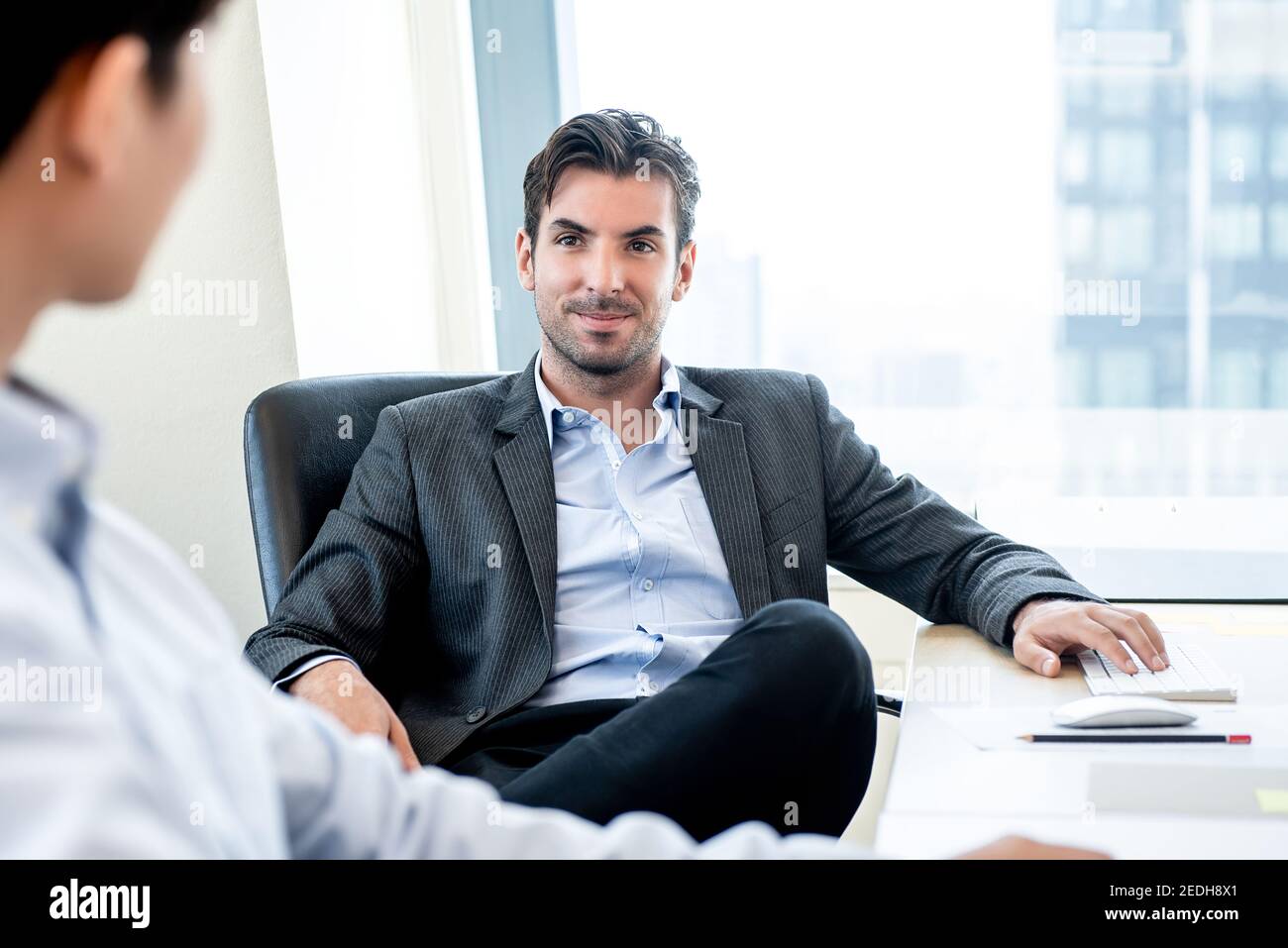 Handsome Hispanic businessman as a boss sitting in a chair listening to his colleague in the office Stock Photo