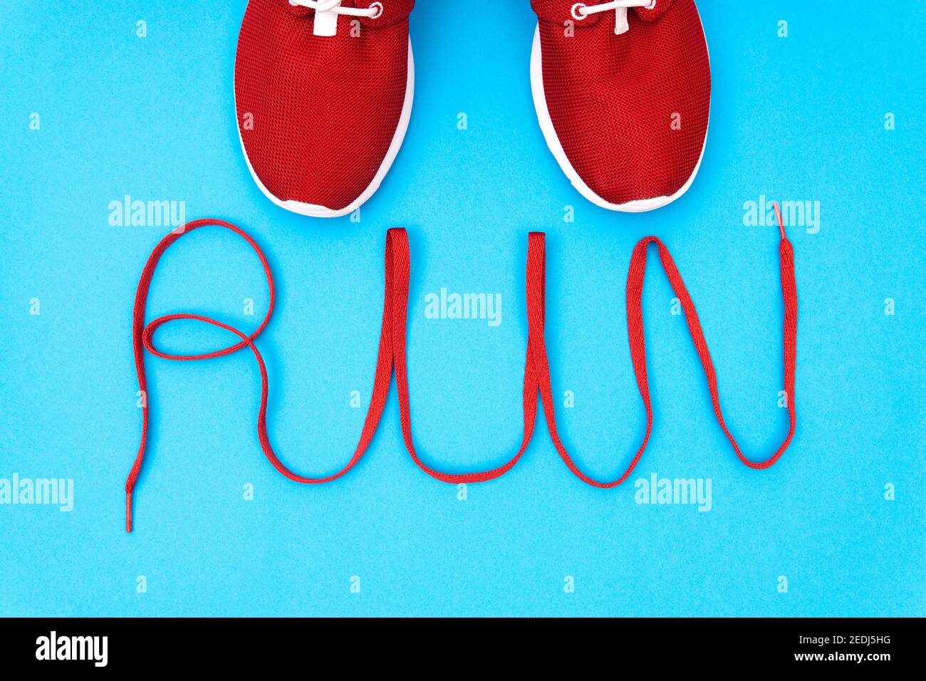 Red running sneakers and lettering 'run' made of a shoelace on a blue background. Creative flat lay, studio shot. Stock Photo