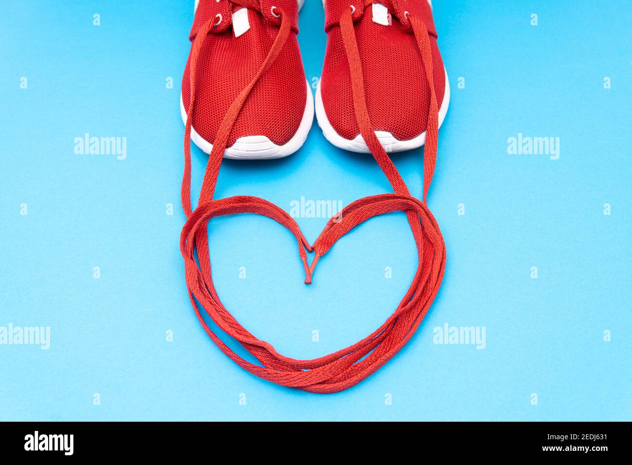 Crop view of red athletic sneakers and a heart symbol made of the shoelaces on a blue background. Running passion creative concept. Stock Photo